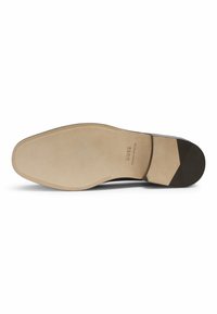 Suola di scarpa elegante con una finitura beige liscia, caratterizzata da un tacco in gomma nera testurizzata e sottili modelli di presa vicino all'area delle dita.