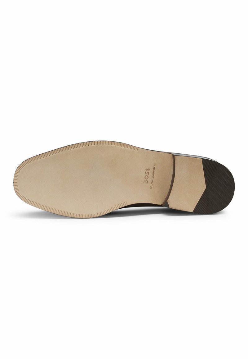 Semelle de chaussure habillée avec une finition beige lisse, dotée d'un talon en caoutchouc noir texturé et de motifs de grip subtils près de la zone des orteils.