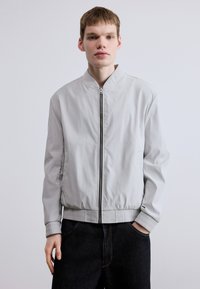 Ανοιχτό γκρι μπουφάν τύπου bomber με όρθιο γιακά, φερμουάρ μπροστά, ριμπ μανσέτες και ελαστική μέση· κατα σκευασμένο από λείο συνθετικό υλικό.