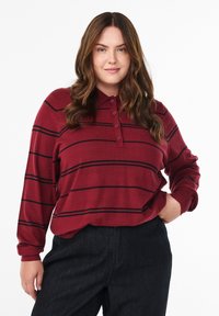 Bordeaux langemouwen polo met zwarte horizontale strepen, voorzien van een kraag en een drieknoopssluiting, gecombineerd met donkere denim broek.