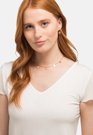 Halskette aus Roségold mit runden Anhängern, zarter Kette und strukturiertem Finish. Getragen zu einem weißen V-Ausschnitt-Shirt aus weichem Stoff.