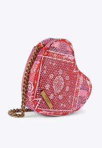 Czerwona torebka w kształcie serca, wykonana z materiału w wzór, z złotym łańcuszkiem. Cechy torebki to teksturowana powierzchnia i logo.