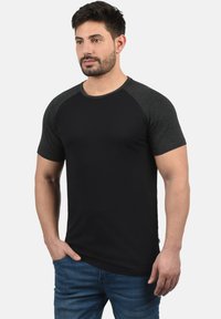 Camiseta negra de manga corta con mangas raglán en gris oscuro, cuello redondo y un diseño ajustado, hecha de una suave tela de mezcla de algodón.