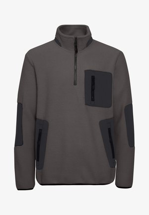 Siv pulover iz flisa z visokim ovratnikom, sprednjim zadrgo na četrt in črnimi akcentnimi nalepkami. Ima dve žepki na zadrgo spredaj.