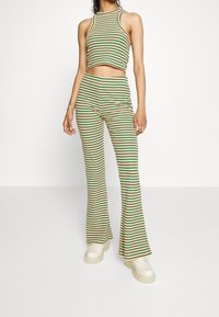 Gestreepte tweedelige outfit bestaande uit een cropped tanktop en uitlopende broek in groen, geel, rood en beige. Het materiaal lijkt ribbelig.