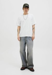 Hvid bomulds t-shirt med korte ærmer, parret med lyse grå denim jeans og brune støvler. Accessoriseret med en mørkegrøn kasket og en sølvkæde.