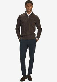 Brun kabelstickad tröja med dragkedja, kombinerad med mörkblå byxor och bruna mockaskor. Outfitten har en skjorta med krage under.