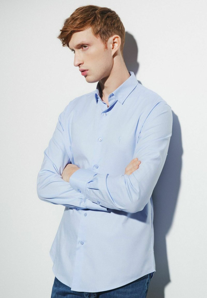 Jasnoniebieska koszula zapinana na guziki wykonana z bawełny, z długimi rękawami, kołnierzykiem oraz subtelnym haftowanym logo na piersi.