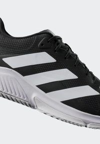 Black athletic shoe with gray accents, featuring a textured upper and three white stripes on the side, designed for performance and comfort.