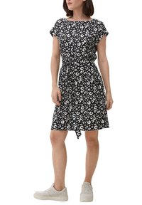 Sukienka w czarno-białą kratkę z krótkimi rękawami i paskiem w talii, z długością do kolan oraz luźnym krojem, zestawiona z białymi trampkami.