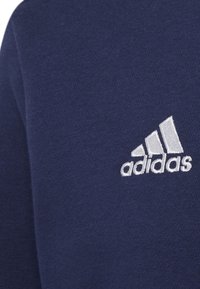 Sudadera de algodón azul marino con el logo de Adidas bordado en blanco y tres rayas inclinadas en el lado inferior izquierdo. Textura suave.