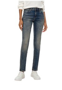 Cienkie dżinsy w wyblakłym niebieskim denonie z delikatnym efektem prania, z średnim stanem i pięcioma kieszeniami. Połączone z białymi trampkami.