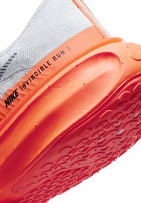 A Nike Invincible Run 3 sneaker szürke felsőrésszel, narancssárga középtalppal és részletes, textúrázott piros külsőtalppal rendelkezik, amely tapadásmintázatokkal van ellátva.