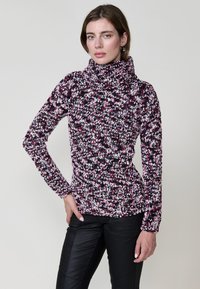 Pull à col roulé en tricot dans des teintes multicolores de rose, noir et blanc. Forme ajustée et texturée avec des manches longues et un détail à ourlet froncé.