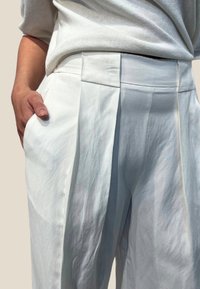 Hvite linbukser med legg, med vid benvidde og en glatt, lett krøllete tekstur. Inkluderer sidelommer og en flat midjebånd.