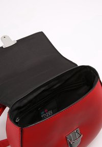 Červená kožená křížová taška s otevřeným černým textilním interiérem a stříbrným uzávěrem, s viditelnou vnitřní kapsou na zip a značkovou etiketou.