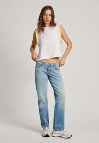 Top corto sin mangas blanco con ribete amarillo, combinado con jeans rectos de pierna clara y zapatillas ligeras.