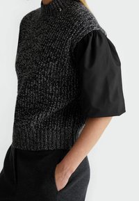 Pletený svetr v šedé a černé barvě s vysokým límcem a nadýchanými krátkými rukávy. Texturovaný vzor na těle, hladká látka na rukávech.