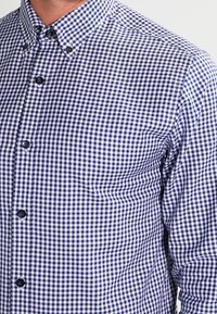 Man wearing a blue and white checkered button-up shirt with a button-down collar, cropped at neck and mid-torso.