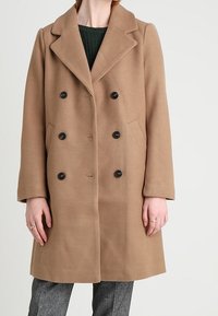 Brun ull dubbelknäppt kappa med stora slag, svarta knappar och sidofickor, med en rak silhuett och långa ärmar.