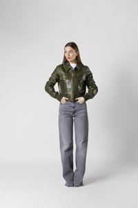 Grön läderjacka med krage, frontdragkedja och två bröstfickor, kombinerad med högmidjade, ljusgrå vida jeans.