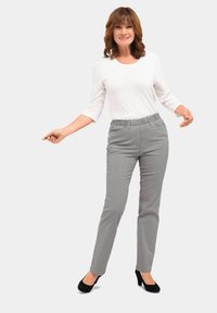 Leichte, graue, elastische Hose mit geradem Schnitt, kombiniert mit einem weißen, drei Viertel langen Langarmshirt. Schwarze Absätze vervollständigen das Outfit.