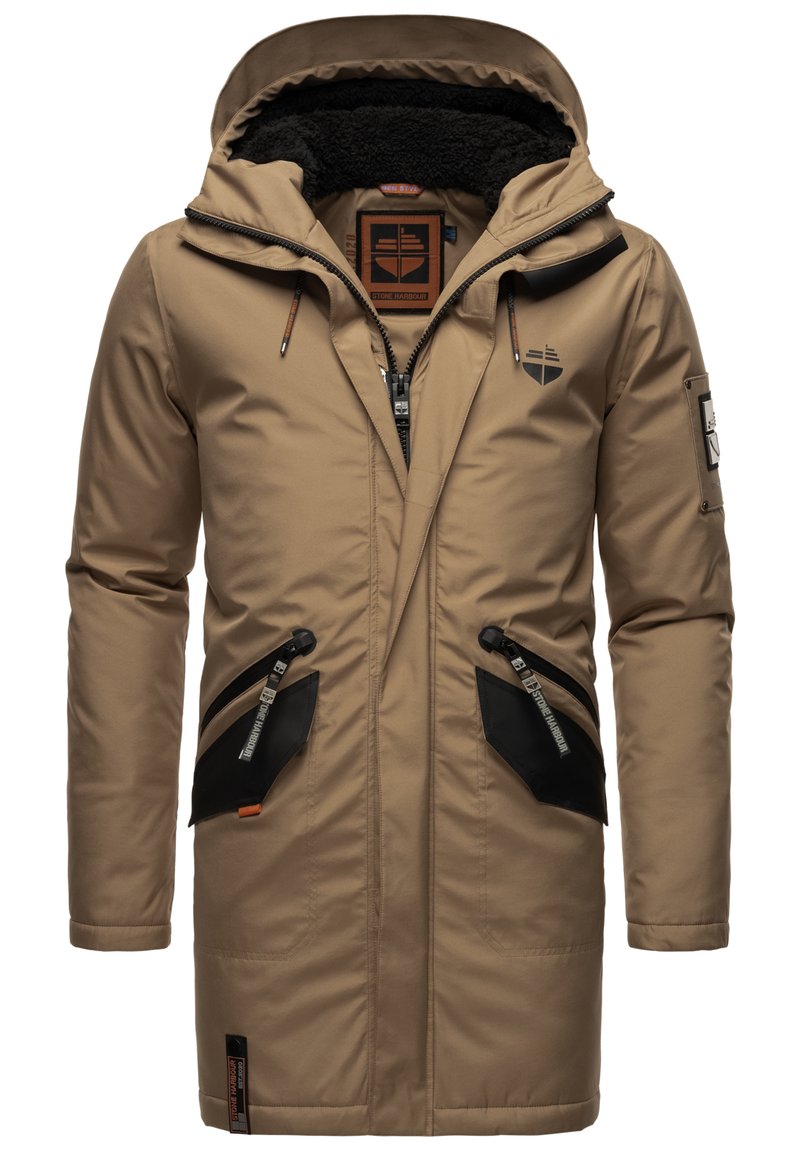 Chaqueta parka beige con capucha forrada de felpa texturizada, bolsillos de acento negros y cierres de cremallera. Presenta un logo en el pecho y tiradores de cremallera únicos.