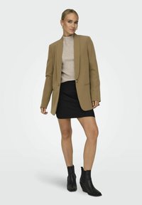 Svetle hnědý blazer se střihovaným střihem, který je kombinován s ribbed béžovým topem a černou mini sukni. Outfit doplňují černé kotníkové boty.