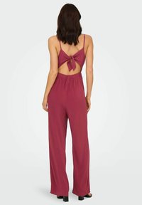 Combinaison bourgogne à fines bretelles, dos nu noué en un nœud, taille élastique et design à jambes larges, fabriquée en matériau doux, longueur mi-cuisse.
