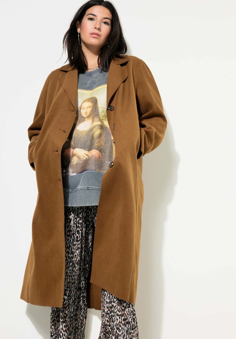 Brown wollen jas met een ontspannen pasvorm, knopen aan de voorkant. Daaronder een graphic sweater met de Mona Lisa, gecombineerd met een patroonbroek.
