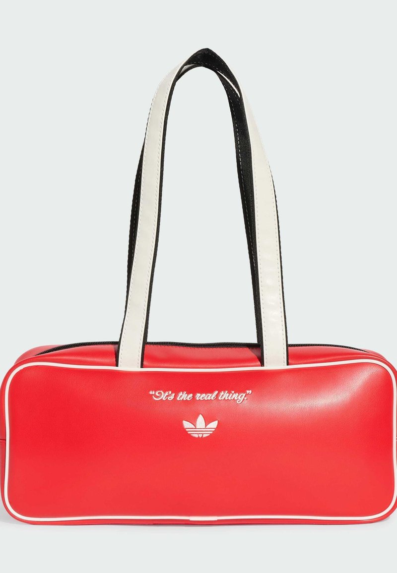 Red rectangular bag with white piping, white handles, and white text "It's the real thing" above the Adidas logo on front side.
