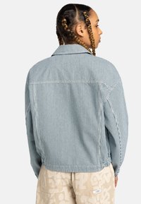Striped denim jacket in light blue and white, featuring a collar and dropped shoulders, with a structured fit and elastic hem.