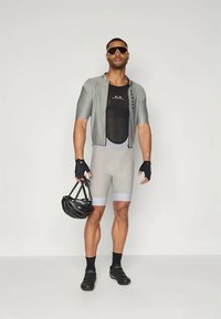 Conjunto de ciclismo que incluye una camiseta ajustada gris, panel de malla y pantalones cortos a juego. Los accesorios incluyen guantes sin dedos y un casco negro.