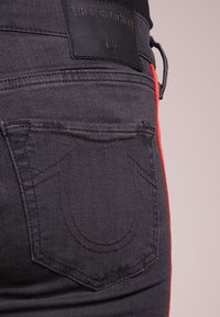 Svarta denimjeans med röda sidostrimmor, utrustade med en True Religion-läderskylt, stickningsdetaljer och snedställda bakfickor.
