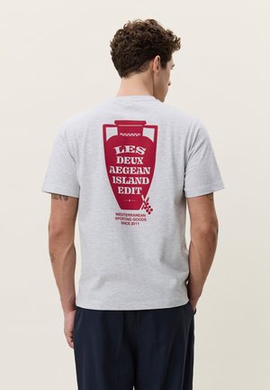 Mann trägt hellgraues T-Shirt mit rotem Amphoren-Grafik und Text, der auf die Ägäische Insel und mediterrane Sportartikel verweist, Ansicht von hinten.