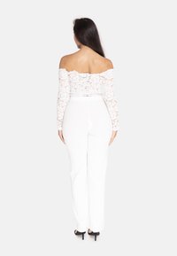 Hvid blonde off-the-shoulder top med lange ærmer, tætsiddende talje, parret med hvide, vide bukser og sorte højhælede sko.