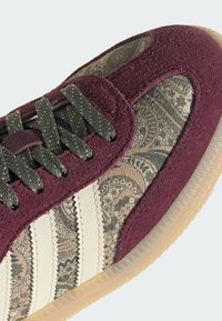 Baskets en daim bordeaux, panneaux en tissu à motif paisley, bandes en cuir crème, lacets texturés gris foncé et semelle en caoutchouc translucide.