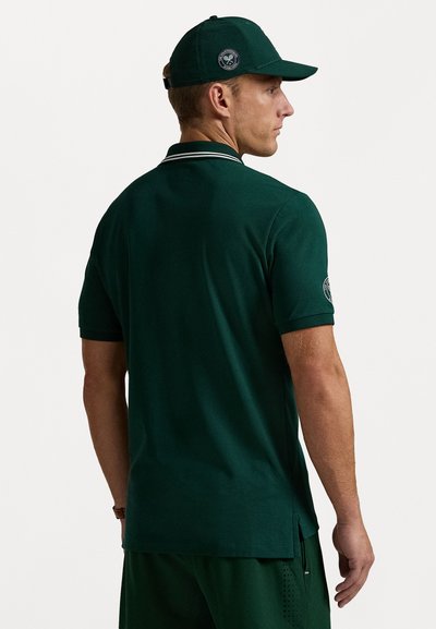 Cămașă polo verde cu mâneci scurte, cu accente albe pe guler și o emblemă pe umăr. Purtați-o cu pantaloni scurți verzi asortați.