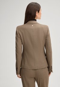Blazer a motivo check marrone con spalline e bottone d'accento argento, caratterizzato da una vestibilità su misura e una finitura in tessuto liscio, visto da dietro.