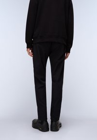 Black sweatshirt with ribbed cuffs, paired with black trousers. Footwear features a smooth texture with a slightly rugged sole.