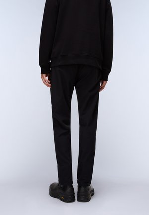 Black sweatshirt with ribbed cuffs, paired with black trousers. Footwear features a smooth texture with a slightly rugged sole.
