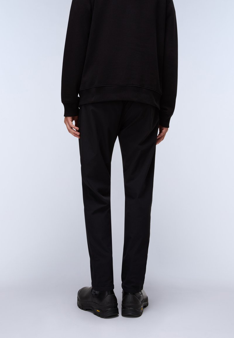 Black sweatshirt with ribbed cuffs, paired with black trousers. Footwear features a smooth texture with a slightly rugged sole.