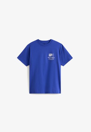 Camiseta de algodón azul de manga corta, con un logotipo gráfico blanco en el lado izquierdo del pecho y la frase "OFF THE WALL" debajo.