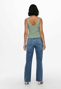 Top verde a costine con scollo a V ampio, abbinato a jeans in denim blu a vita alta svasati con orlo grezzo e tasche posteriori.