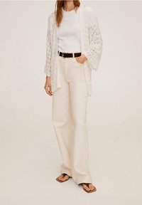 Bílý krajkový cardigan na bílé triko, doplněný béžovými širokými kalhotami a hnědými žabkami, se černým opaskem pro kontrast.