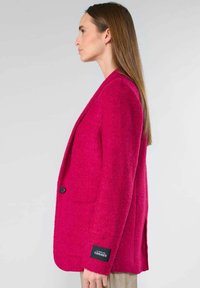 Roze tweed blazer met een enkele knoop, zijzakken en een merkpatch op de mouw. Getailleerde pasvorm met geknipte revers.