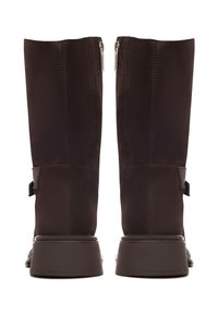 Botas de ante marrón hasta la rodilla con acabado texturizado, que cuentan con una suela marrón lisa, cremalleras laterales y un acento de correa cerca del tobillo.