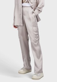 Satin-Cargo-Hosen in Hellgrau mit seitlichen Taschen, lockerer Passform und glatter Textur. Kombiniert mit weißen Sneakers.