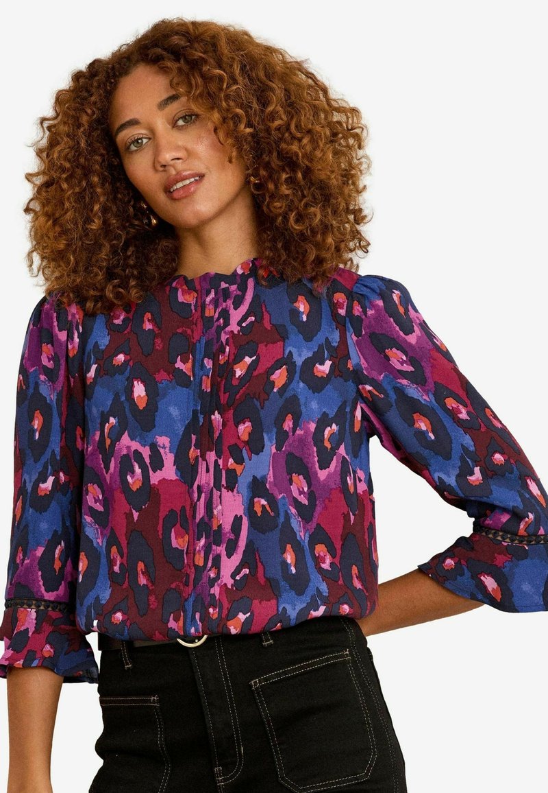 Krāsaina, rakstaina blūze ar purpura, zila un rozā dzīvnieku apdruku, ar augstu apkakli un nedaudz pūkainām piedurknēm. Tekstūrēts audums.