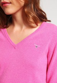 Pull en v rose en tissu doux et texturé. Présente un petit logo brodé sur la poitrine.